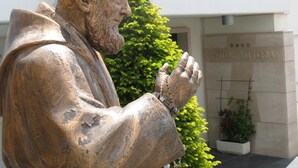 A statue of a man in a suit with a cross behind him, in front of a building labeled "HOTEL VITTORIA". - Vittoria (San Giovanni Rotondo)