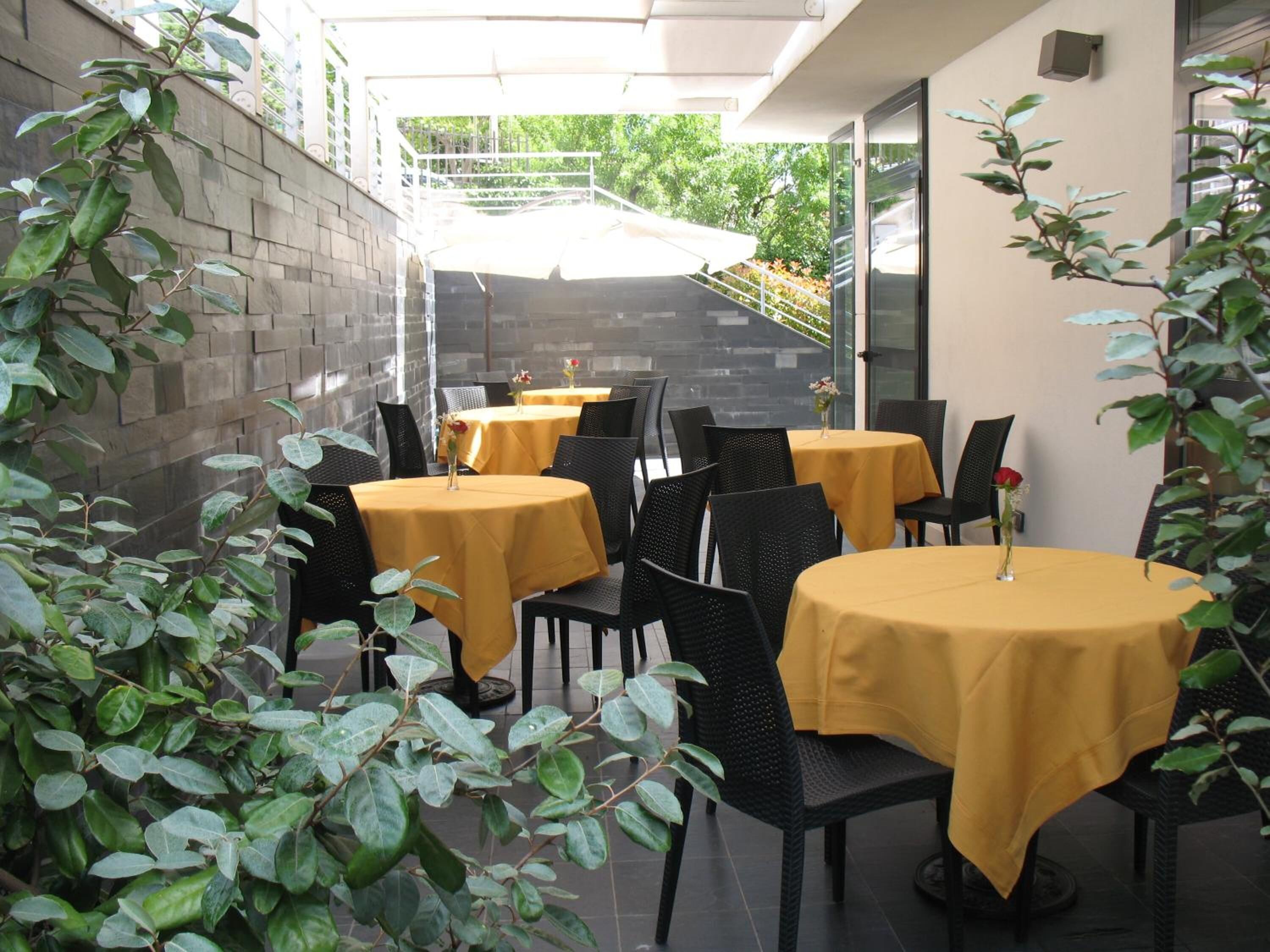 Eine Terrassensitzgruppe mit runden Tischen, bedeckt mit gelben Tischdecken, umgeben von schwarzen Stühlen.