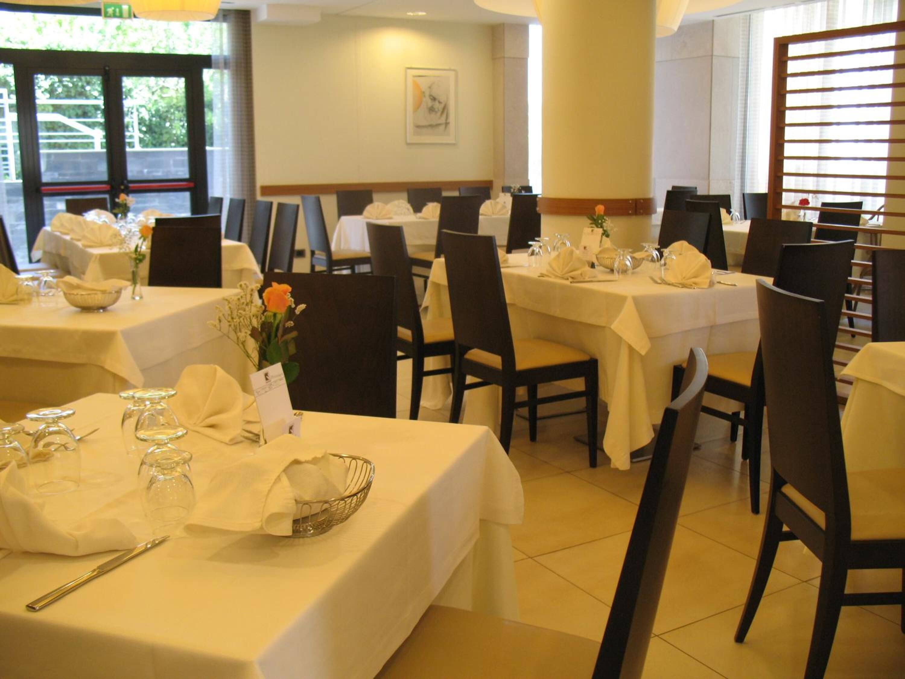 A restaurant with multiple tables set for dining, each with a white tablecloth, chairs, and basic table settings including cutlery and napkins.