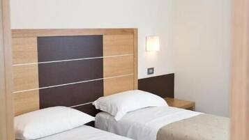 A hotel room with two single beds, each with a wooden headboard and white bedding.