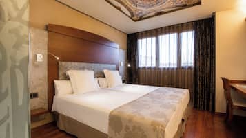 Ein Hotelzimmer mit einem großen Bett, einem Holz-Kopfteil, einem Schreibtisch und einer dekorativen Decke.