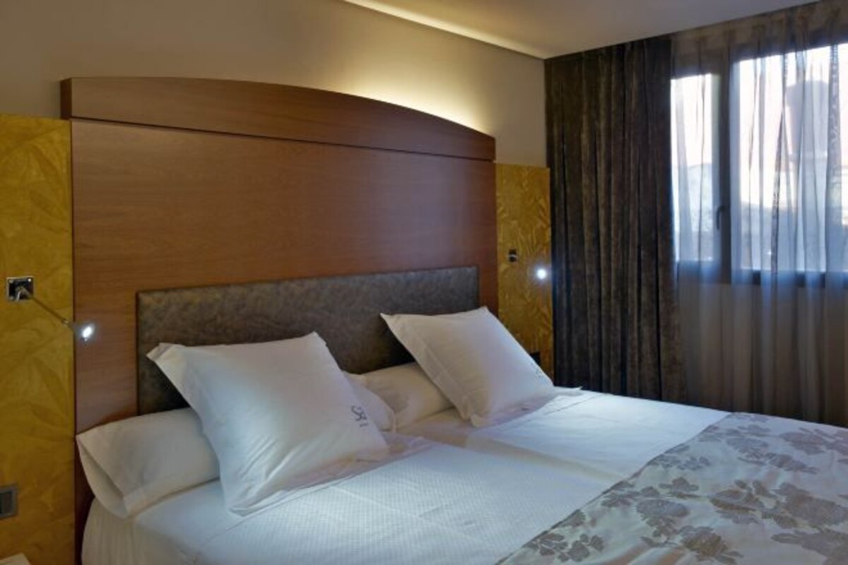 Una habitación de hotel con una cama grande, cabecera de madera y una ventana con cortinas.