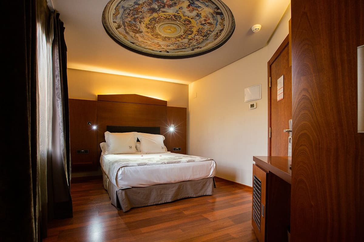 Habitación de hotel con una cama grande, suelo de madera, techo con un diseño detallado y un armario de madera.
