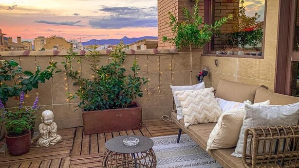 A rooftop terrace with a cushioned seating area, potted plants, and a decorative Buddha statue.
