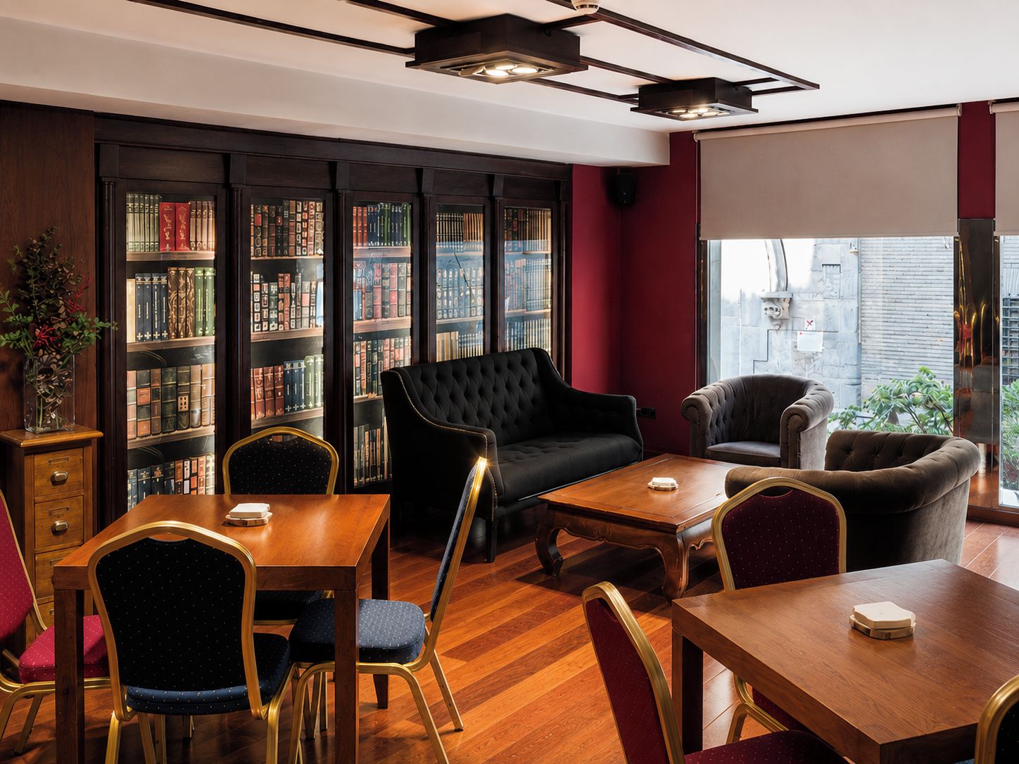 Una biblioteca con estanterías, un sofá negro y un comedor con mesas y sillas de madera.