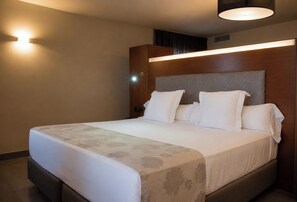 A hotel room with a bed, a headboard, and a wall-mounted light fixture. - Hotel Sancho Abarca Petit SPA (Huesca)