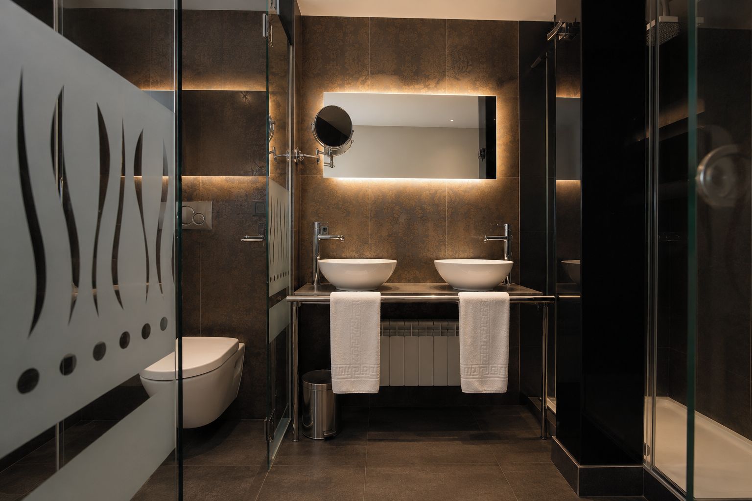 Un baño moderno con cabina de ducha de vidrio, dos lavabos, inodoro y un espejo grande.
