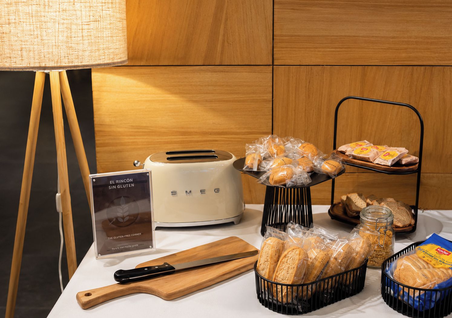 A table with a toaster, a bread basket, a bread tray, a knife, a cutting board, and a sign about gluten-free products.