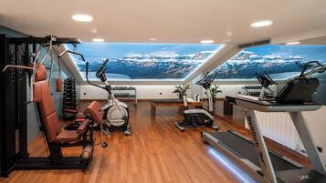 Un gimnasio con diversos equipos de ejercicio, incluyendo cintas de correr, elípticas y máquinas de pesas, con un amplio ventanal que ofrece vistas a la montaña.