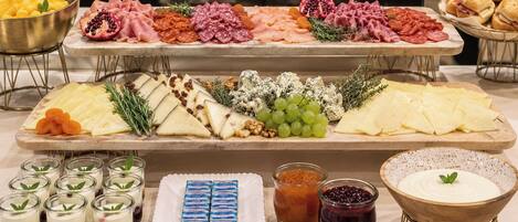A buffet with various cheeses, meats, fruits, and desserts.