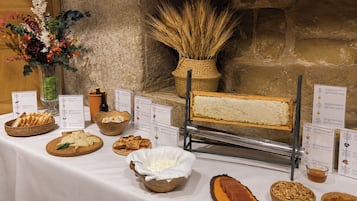 Una mesa de buffet con diversos alimentos, incluyendo queso, pan y un cortador de pan.