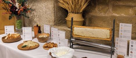 A buffet table with various food items, including cheese, bread, and a bread slicer.