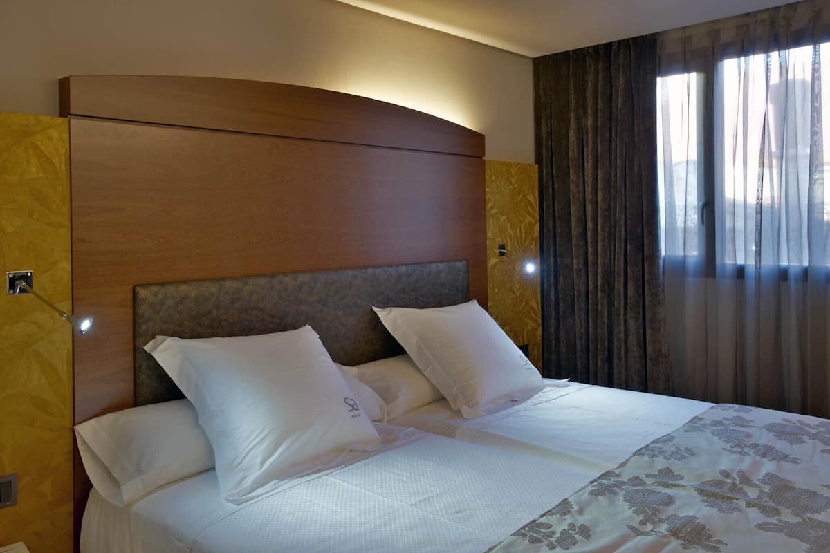 Una habitación de hotel con una cama grande, un cabecero de madera y una ventana con cortinas.