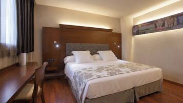 A hotel room with a bed, bedside table, chair, and a painting on the wall.