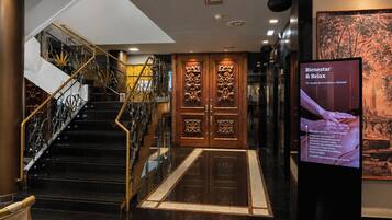 Eine Hotelhalle mit Treppe, einer Rezeption und einer digitalen Infotafel.