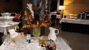 A dining table set with wine glasses, a bottle of IdRIS, a vase with flowers, a teapot, and a pitcher. - Hotel Sancho Abarca Petit SPA (Huesca)