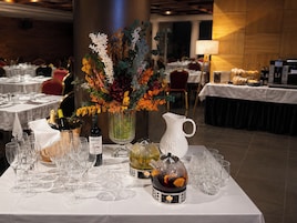 Una mesa de comedor dispuesta con copas de vino, una botella de IdRIS, un florero con flores, una tetera y una jarrón.