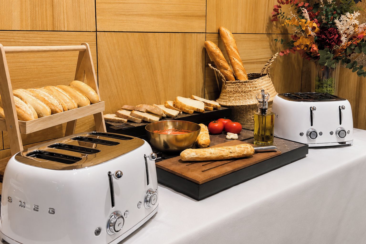 Un plan de travail de cuisine avec deux grille-pain, un présentoir à pain, un panier de pain, un bol de sauce tomate, des tomates, de l’ail et une planche à découper.