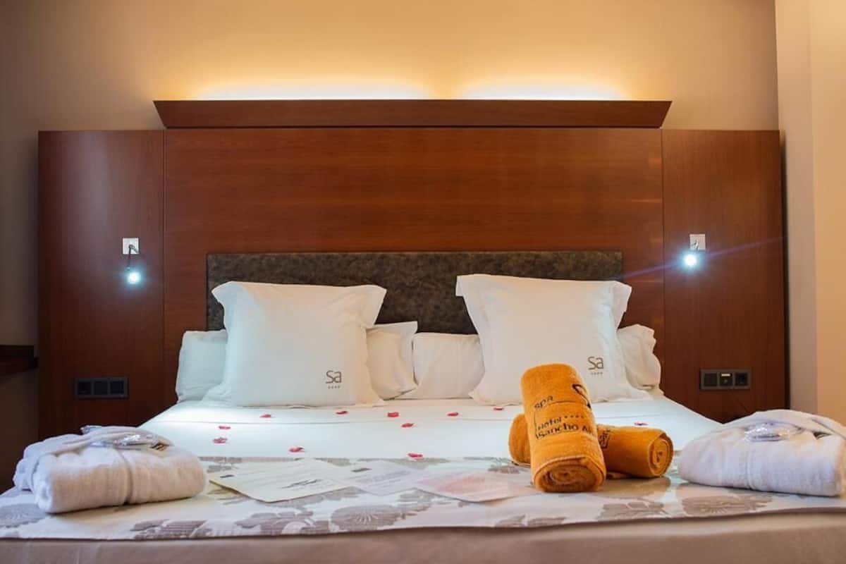 Una cama bien hecha con sábanas blancas, cabecero, toallas y un pequeño folleto sobre la cama.