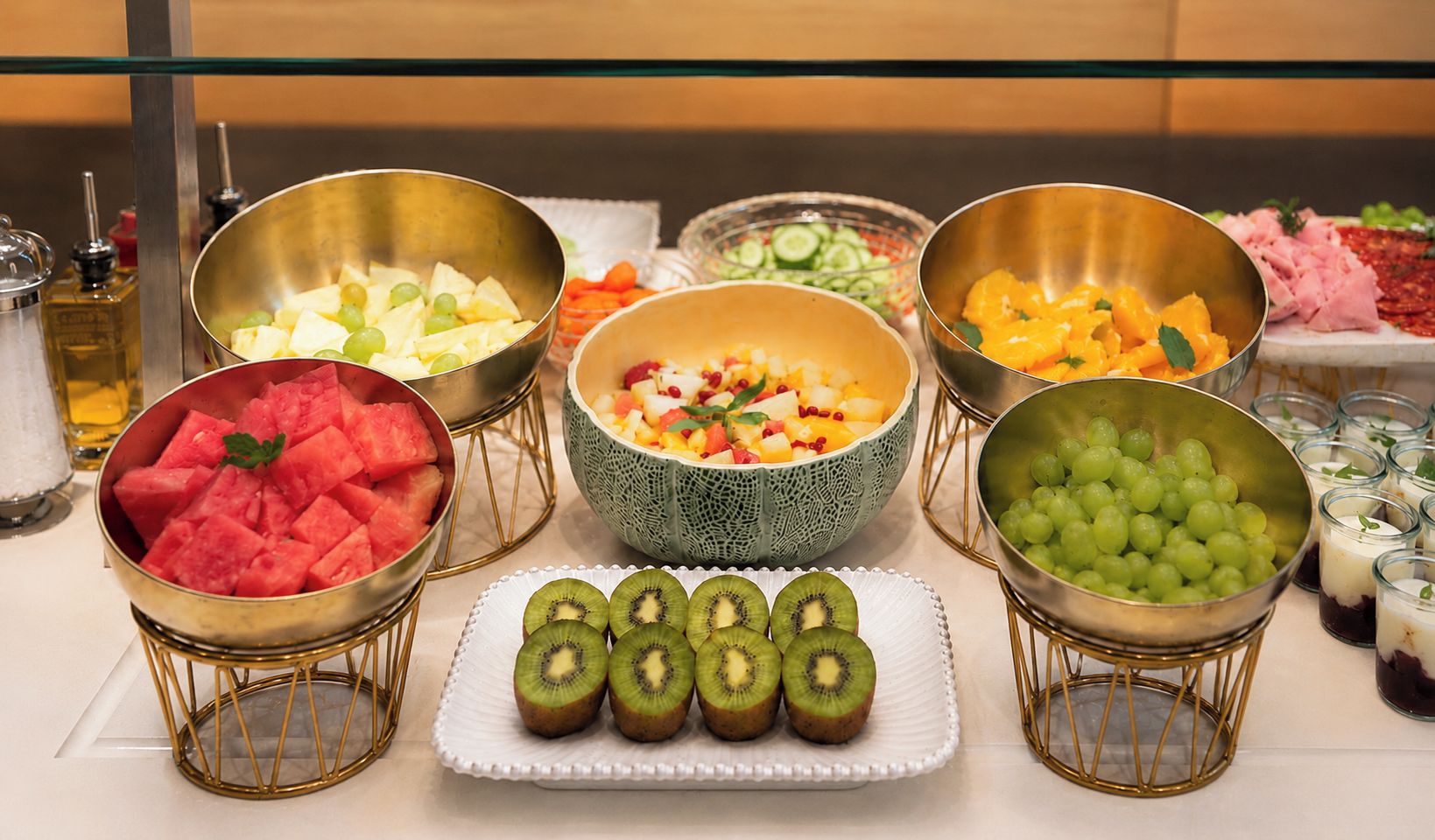 Een buffettafel met diverse soorten eten, zoals watermeloen, druiven, kiwi en een fruitsalade.