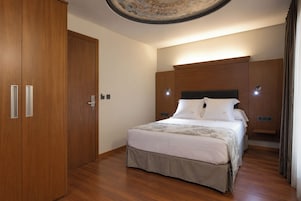 Habitación de hotel con un armario de madera, una cama con ropa blanca y una lámpara fijada a la pared.