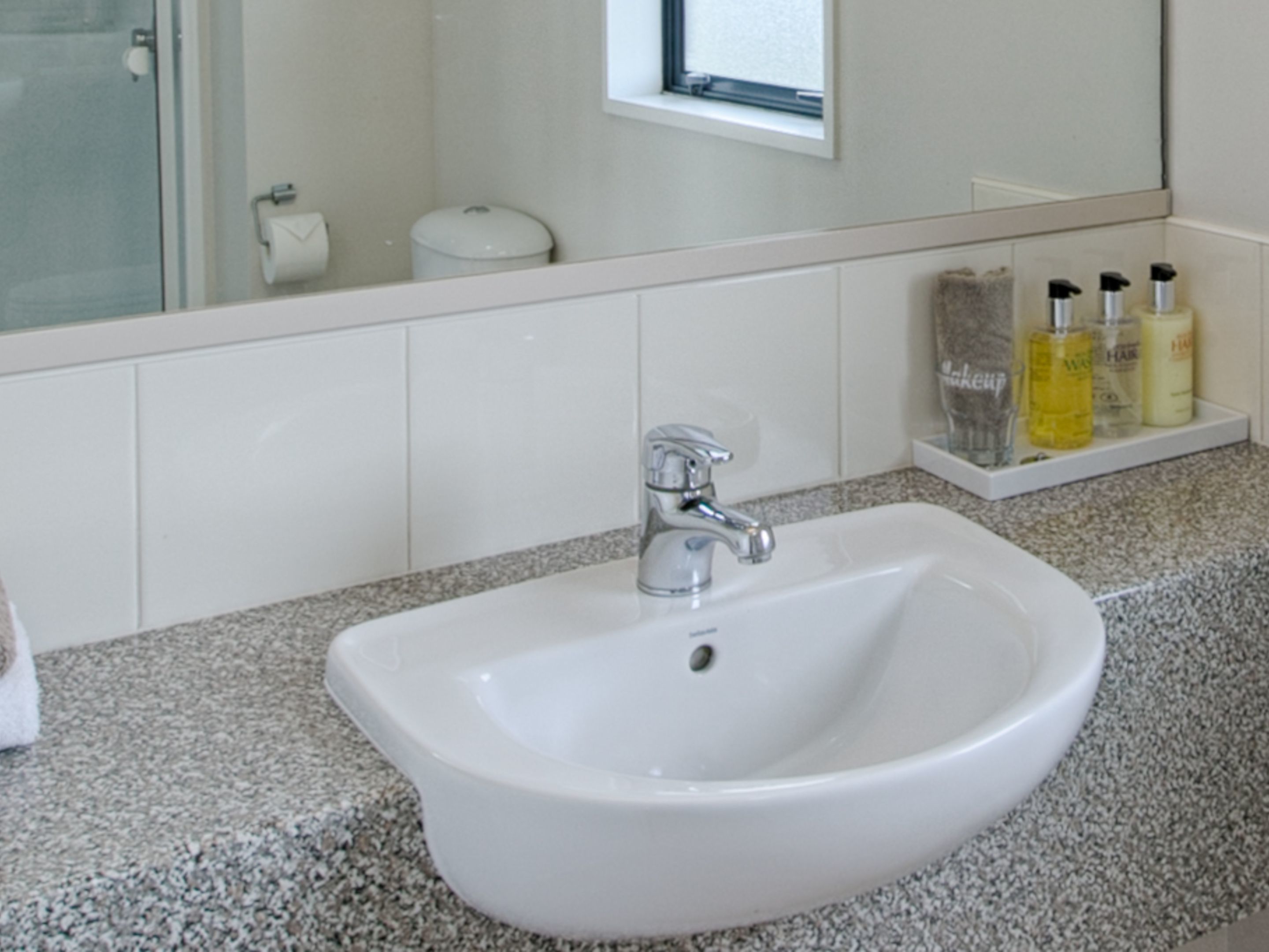A bathroom with a white sink, a mirror, and a shelf with toiletries.