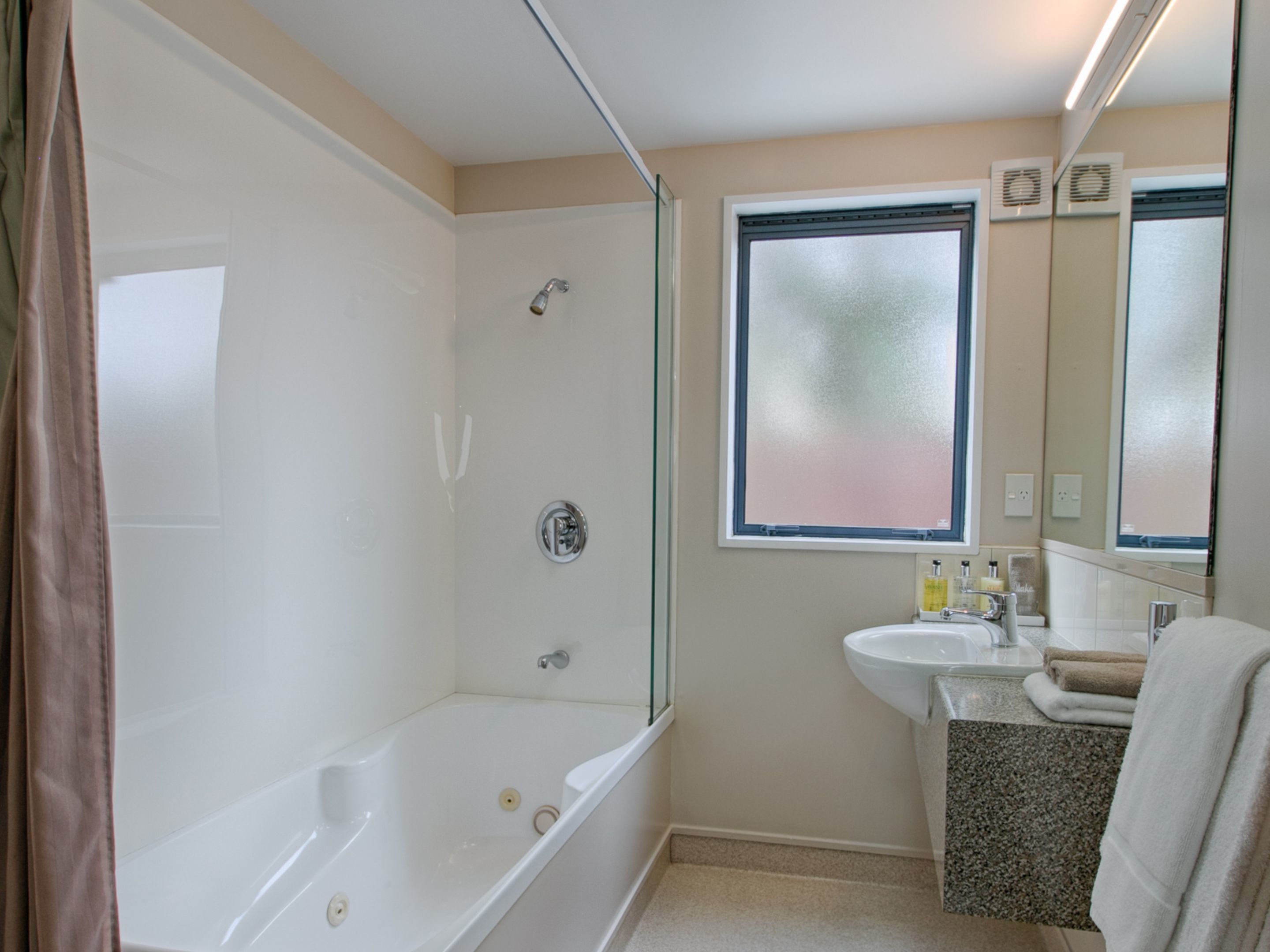 Un baño con bañera, ducha, lavabo y ventana con vidrio esmerilado.