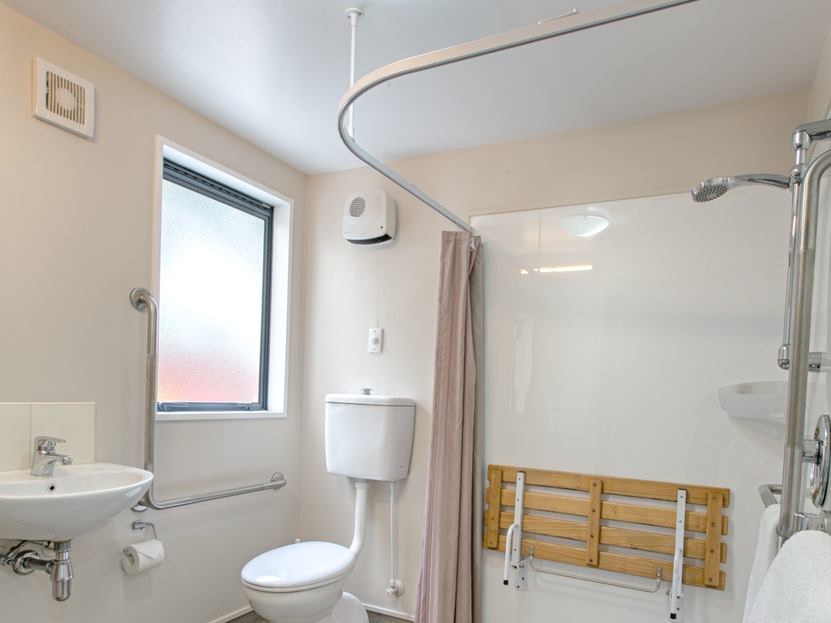 A bathroom with a toilet, sink, shower, and window.