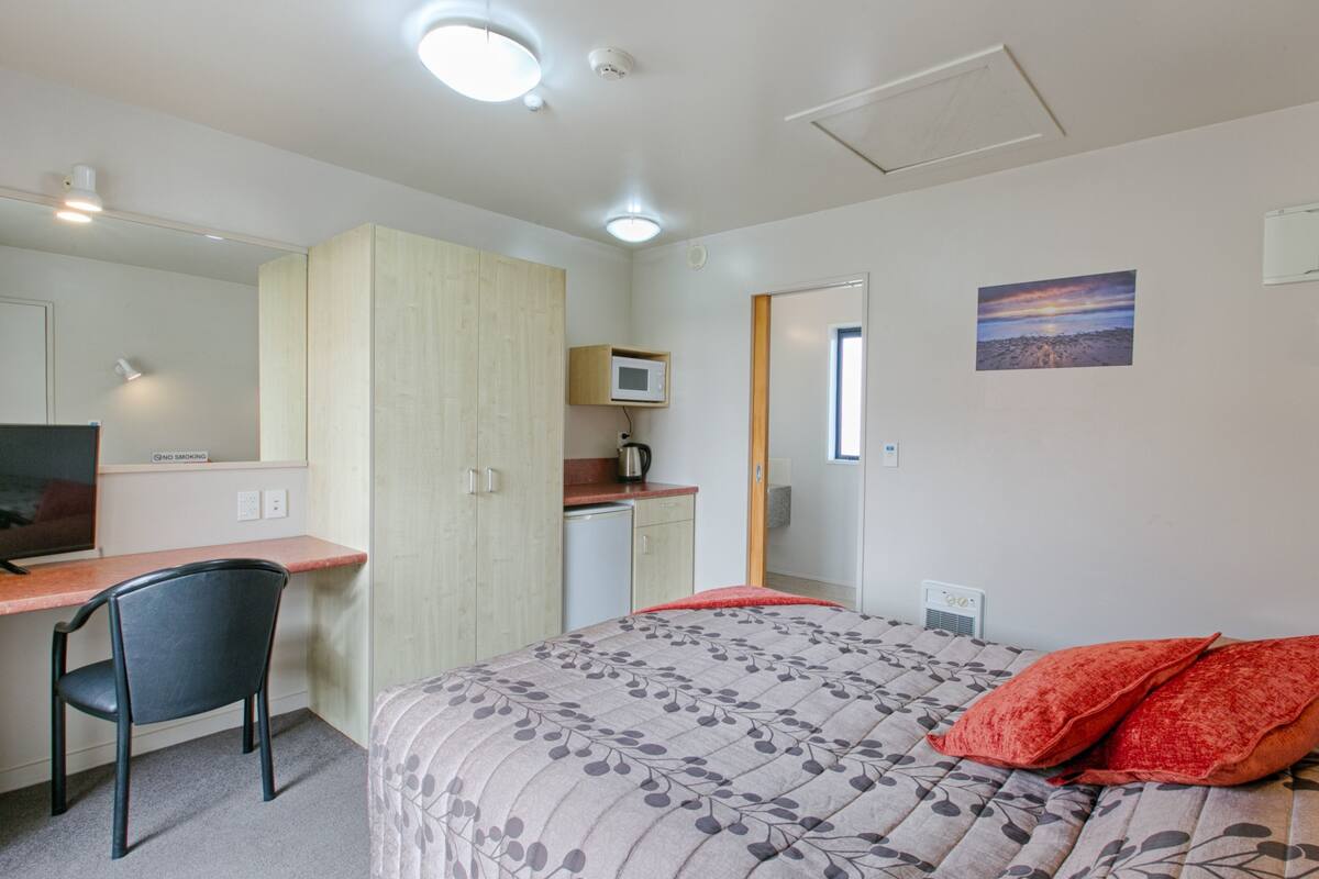Une chambre avec un lit, un bureau, une chaise, un four à micro-ondes et une petite kitchenette.