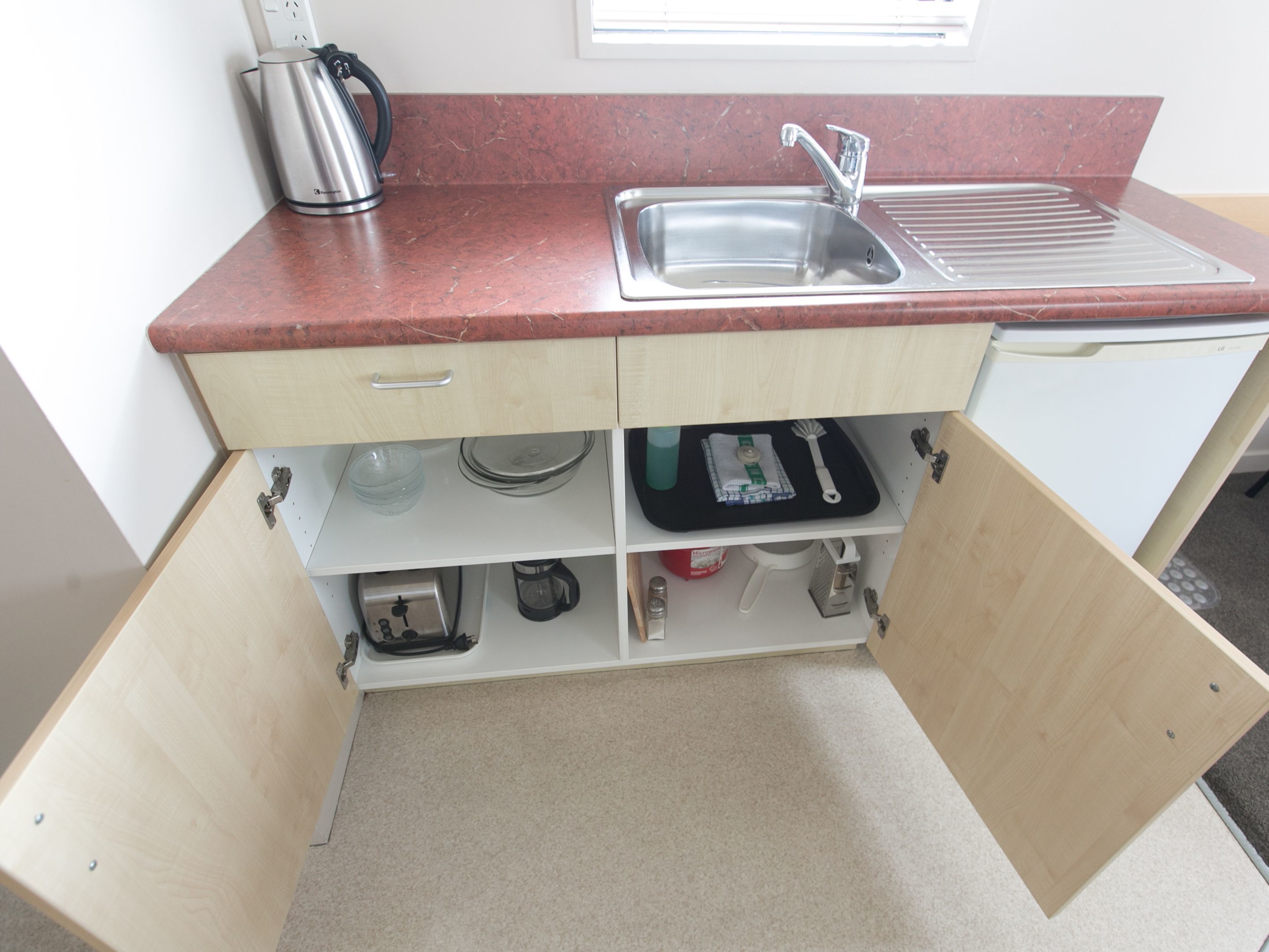 A compact kitchen with a sink, a kettle, and various utensils stored in drawers.