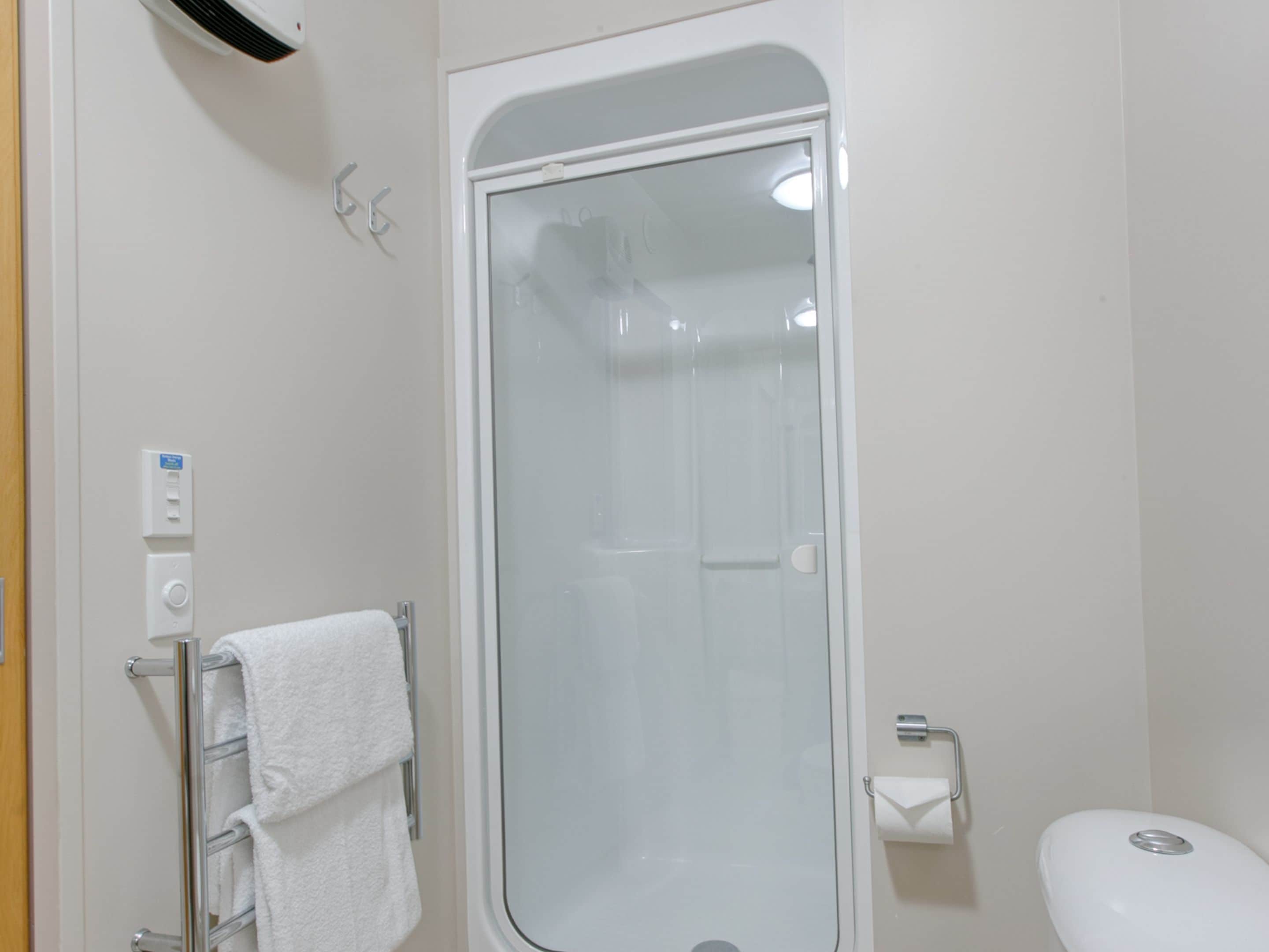 A bathroom with a glass-enclosed shower, a towel rack with a white towel, a toilet, and a wall-mounted light switch.