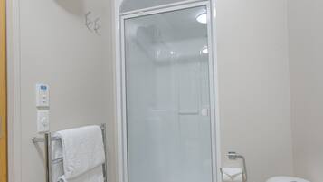 A bathroom with a glass-enclosed shower, a towel rack with a white towel, a toilet, and a wall-mounted light switch.