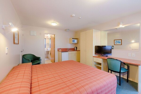 Una habitación de hotel con cama, escritorio, televisión, silla y kitchenette.