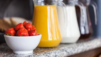 A bowl of strawberries, a pitcher of orange juice, and a pitcher of milk on a countertop.