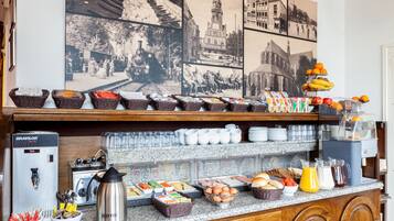 A buffet setup with various food items and beverages, including baskets of fruits, a coffee machine, and a juice dispenser.