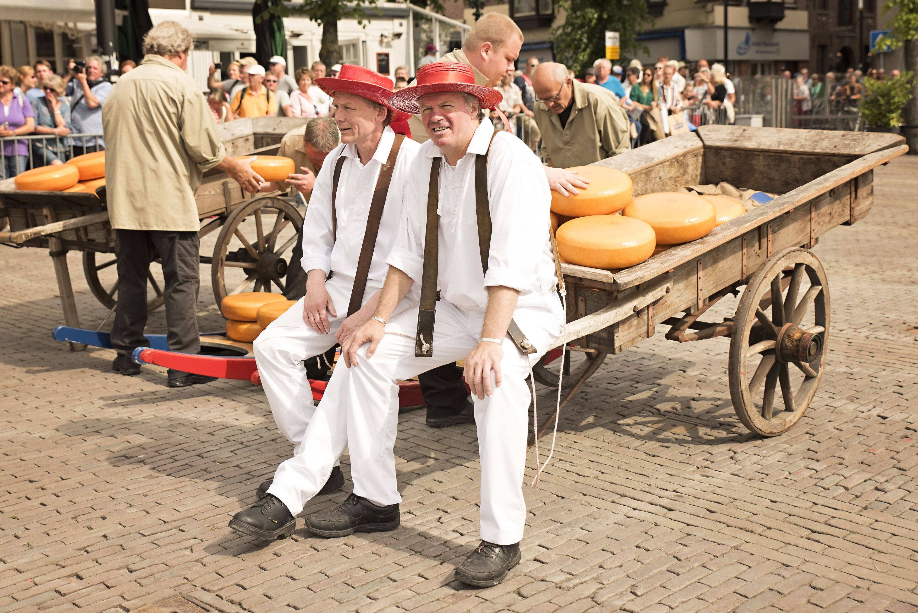 A group of people in traditional attire sitting on a wooden cart with orange cushions.