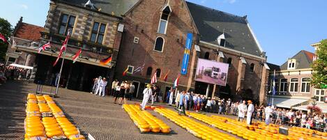Un bâtiment historique doté d’un imposant clocher et devant lequel se trouve un marché où sont exposées des meules de fromage.