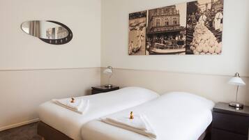 A hotel room with a double bed, a nightstand, a lamp, a mirror, and a wall with a black and white photograph.