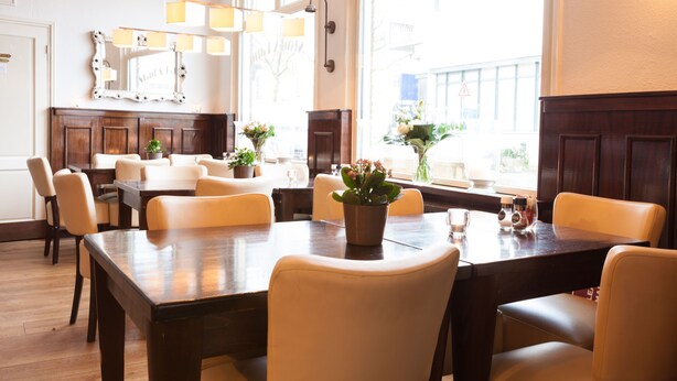 A dining area with a large wooden table, several chairs, and potted plants. - Hotel Stad en Land (Alkmaar)