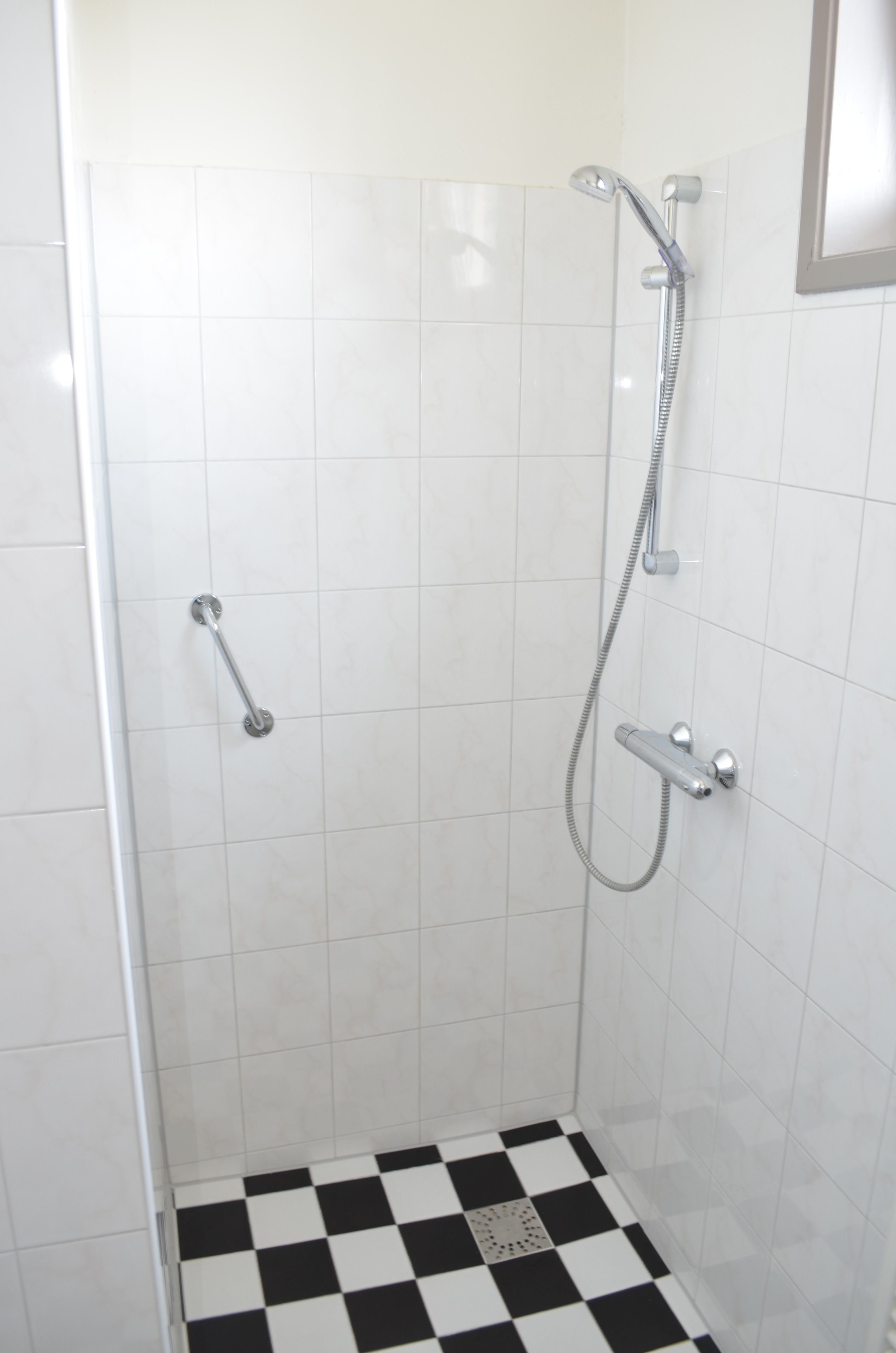 A small, enclosed shower area with a checkered floor, a handheld showerhead, and a handheld shower attachment.