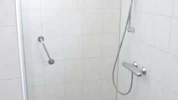 A small, enclosed shower area with a checkered floor, a handheld showerhead, and a handheld shower attachment.
