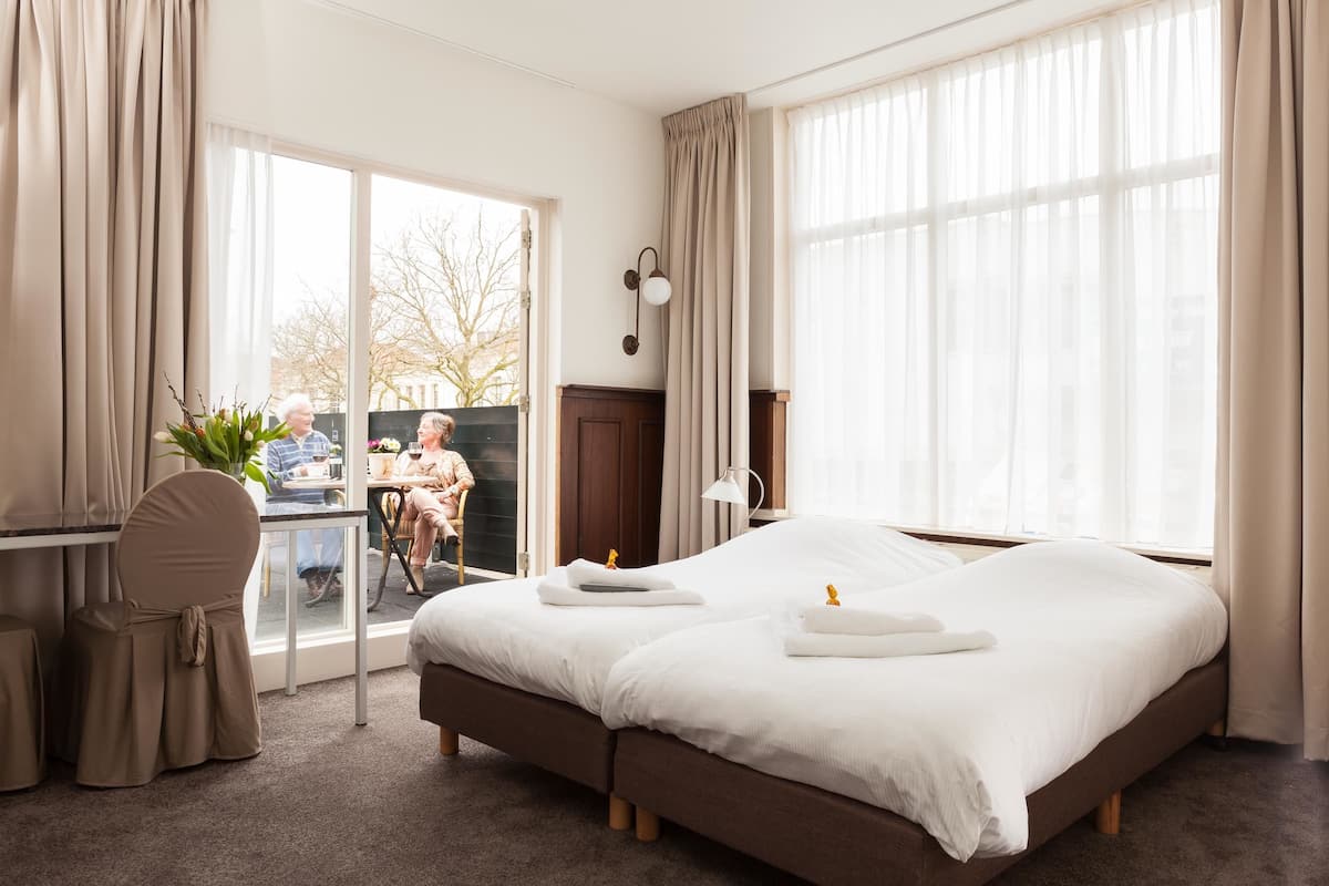 A hotel room with a large bed, a desk with a chair, and a view of the outside.
