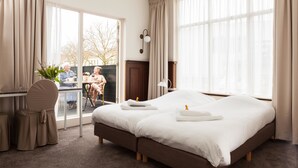 A hotel room with a large bed, a desk with a chair, and a view of the outside. - Hotel Stad en Land (Alkmaar)