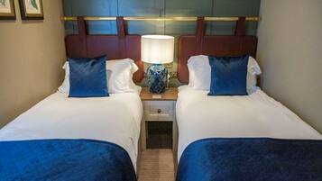 A hotel room with two beds, a nightstand with a lamp, and a headboard with a decorative panel.