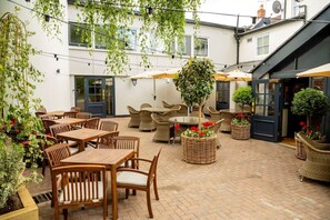 An outdoor patio with wooden tables and chairs, wicker planters with red flowers, and hanging plants. - The Globe, Warwick, Warwickshire - Brunning & Price (Warwick)