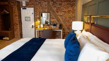 A hotel room with a brick wall, a desk with a mirror, a bed with blue and white bedding, and a wooden headboard.