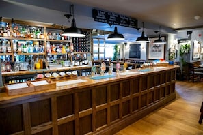 A bar area with a wooden counter, multiple bottles, and a menu board. - The Globe, Warwick, Warwickshire - Brunning & Price (Warwick)