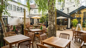 An outdoor seating area with wooden tables and chairs, surrounded by trees and a building labeled 'The Globe Free House'. - The Globe, Warwick, Warwickshire - Brunning & Price (Warwick)
