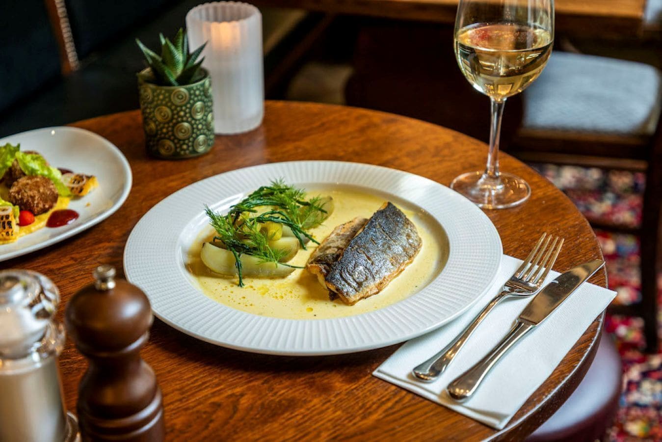 A dining table with a plate of fish, a glass of wine, and a candle.
