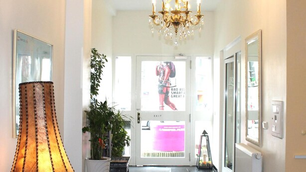 A hotel lobby with a chandelier, a large lamp, potted plants, and a door with a poster. - Hotel Famosa (Düsseldorf)